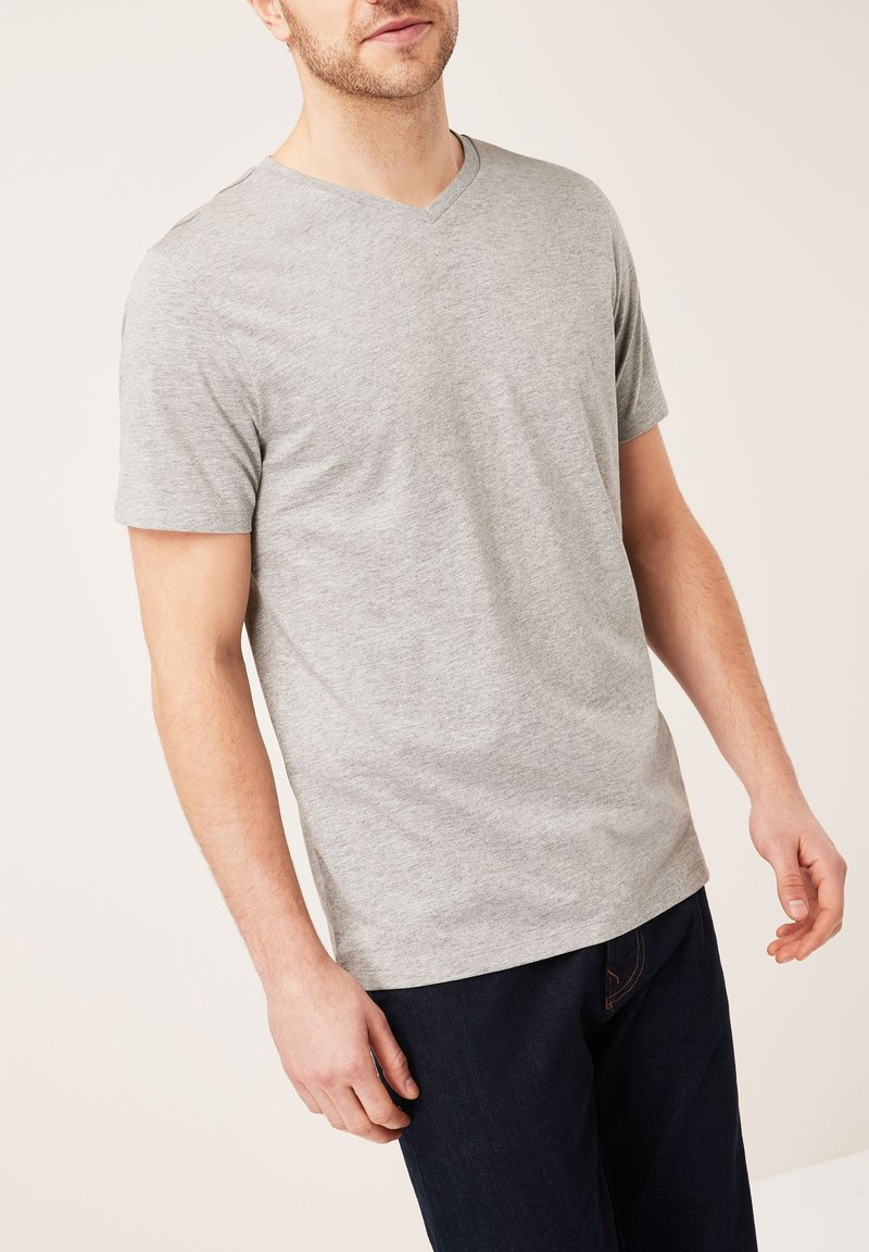 Graues V-Ausschnitt-T-Shirt aus weichem, strukturiertem Stoff mit kurzen Ärmeln, kombiniert mit dunklen Jeans, präsentiert vor einem neutralen Hintergrund.
