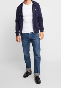 Marinblå zip-up huvtröja med en framficka, tillsammans med en vit crewneck t-shirt och mellanblåjeans, med uppvullade ärmslut och svarta loafers.