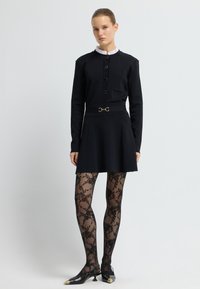 Černé šaty s vysokým límcem, předními knoflíky a přiléhavým pasem. Nosené s průhlednými černými punčochami s květinovým vzorem a černými botami s špičatou špičkou.