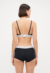 Svart bralette med justerbara remmar och ett vitt randigt band, kombinerad med svarta boyshorts med ett vitt randigt midjeband.