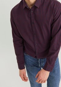 Långärmad skjorta med knappar i mörkröd och marinblå rutmönster, tillverkad av tyg med en mjuk textur; kombinerad med bl å denimjeans.