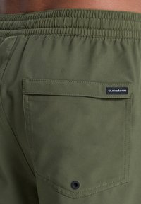 Λαδί σορτς με ελαστική μέση, με πίσω τσέπη με τετράγωνο καπάκι και μικρή μαύρη ετικέτα λογότυπου. Λείος υφής.