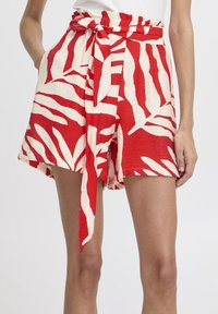 Shorts à motifs rouges et blancs avec une ceinture à nouer, présentant une coupe ample et un imprimé feuilles sur un tissu léger.