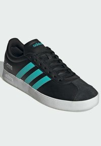 Sorte sneakers med tre teal striber, struktureret sort overdel, snørelukning og hvid gummisål. Har branding på siden.