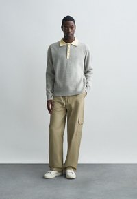 Grijze geribbelde trui met een crèmekleurige polo-kraag en knoopsluiting, gecombineerd met beige wijde cargobroek en witte sneakers.