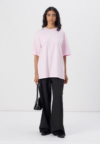 Růžové oversized tričko s krátkými rukávy, kombinované s černými kalhotami širokého střihu a černými botami. Oblečení má jednoduchý design a měkkou látku.