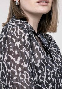 Blouse transparente noire et blanche avec un motif léopard, fermeture à boutons et texture douce, dotée d'un col et de manches courtes.