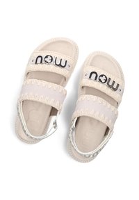 Sandali beige chiaro con due ampi cinturini in tessuto decorati con la scritta nera "now", una cinghia di regolazione sul tallone in argento e una suola texture.