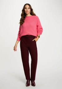 Maglione in maglia fucsia con scollo ampio, abbinato a pantaloni bordeaux sartoriali con vita cinturata. Texture liscia e design attillato.