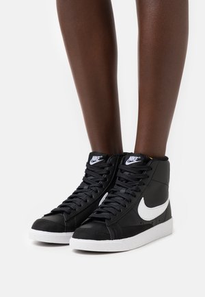 Svarta höga sneakers med vita detaljer, tillverkade av slätt syntetiskt material. Har snören och en texturerad tåhätta.