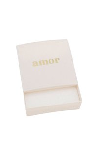 Scatola bianca con una finitura liscia e opaca e un coperchio curvo. La parola "amor" è stampata in un sottile carattere dorato sul fronte. Aprendo la scatola si scopre un interno vuoto.