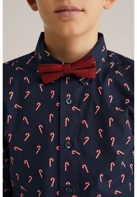 Marinblå skjorta med rött och vitt polkagrismönster, med en matchande vinröd fluga och blå knappar framtill.