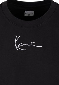 Sweat-shirt noir à col rond avec broderie blanche cursive "Karl" centrée sur la poitrine et une étiquette de taille visible à l’intérieur du col.