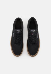 Musta kangastennarit pyöreällä kärjellä, nauhallinen malli, sivussa valkoinen ja punainen erottuva bränditunniste sekä ruskea kumipohja.