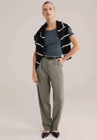 Pantaloni gri cu talie înaltă, ajustați la talie, asociați cu un top albastru cu mânecă scurtă. Un pulover dungat alb-negru aruncat pe umeri. Pantofi negri cu vârf ascuțit.