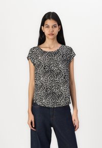 Top corto de manga corta en blanco y negro con un patrón abstracto texturizado, cuello redondeado y un ajuste relajado, combinado con pantalones de mezclilla oscuros.