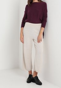 Pull bordeaux à manches longues, associé à un pantalon large en crème à motif chevrons et des chaussures noires à lacets. Textures douces visibles.