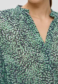 Shirt met een marineblauwe achtergrond en een groen-witte abstracte zigzagpatroon, gemaakt van lichtgewicht stof met een V-hals en een zachte textuur.