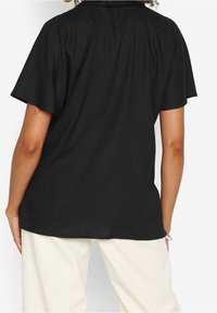 Černá krátká rukávová košile s volným střihem. Hladká látka, zakřivený lem a jemné řasení na ramenním švu. Nosit s kalhotami světlé barvy.