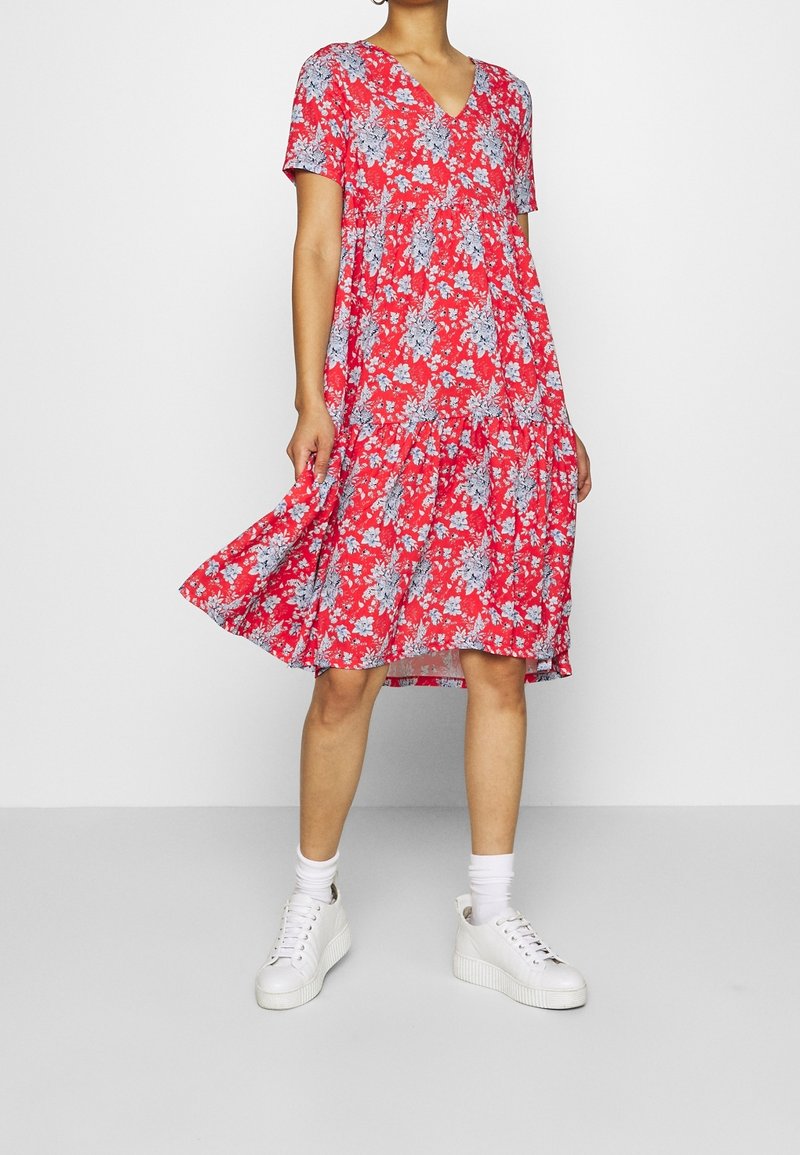 Robe à fleurs rouges avec des manches courtes, un décolleté en V et une jupe à volants. Motif floral bleu et blanc, associée à des baskets blanches et des chaussettes de cheville.