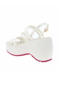 Sandali piatti bianchi con molteplici cinturini sottili. Presentano una suola in gomma rosa e una chiusura con fibbia, evidenziando un design con punta arrotondata.