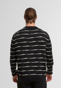 Maglione nero con strisce orizzontali bianche, scollo rotondo e polsini e orlo a costine. Tessuto liscio, pesantezza media.