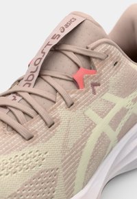 Lichtroze hardloopschoen met een gestructureerde mesh bovenkant, siliconen veterslinger, en een witte zool. Kenmerkt zich door het ASICS-logo en een onderscheidend patroon.