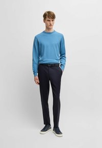 Light blue sweater with round neck, paired with navy trousers. Model wears dark sneakers. Simple design, smooth texture, and no visible patterns.