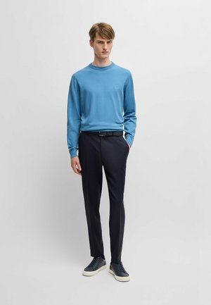 Lichtblauwe trui met ronde hals, gecombineerd met marineblauwe broek. Model draagt donkere sneakers. Eenvoudig ontwerp, gladde textuur en geen zichtbare patronen.