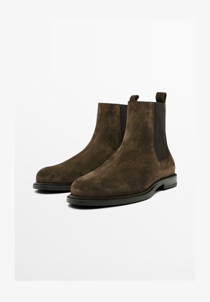 Koffiekleurige suede Chelsea-boots met elastische zijkanten en trekflappen, featuring een ronde neus en een zwarte rubberen zool. Over het geheel gladde textuur.