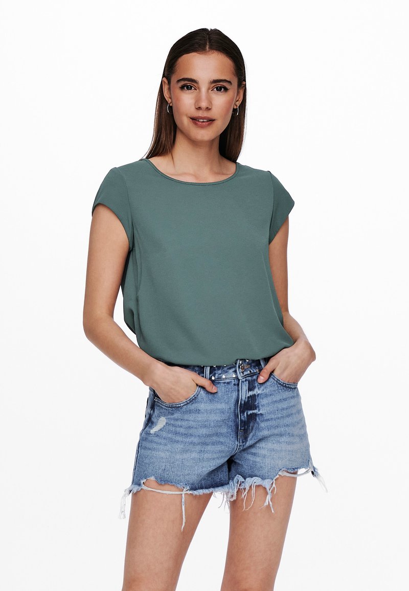 Grünes, kurzärmeliges Oberteil mit rundem Ausschnitt, kombiniert mit verwaschenen Denim-Shorts. Glatte Textur und lockere Passform.