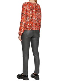 Rode en zwarte slangenprint langemouwen top, gecombineerd met strakke grijze neplederen broek en zwarte plateau schoenen.