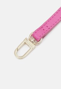 Cinturino in pelle rosa con chiusura in metallo dorato incisa con "Ted Baker" su uno sfondo bianco.