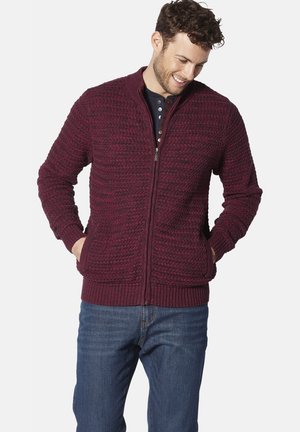 Burgunderfarbener Reißverschluss-Pullover mit strukturiertem Strickdesign, gerippten Bündchen und Saum, seitlichen Taschen, getragen über einem marineblauen Hemd, kombiniert mit blauen Jeans.