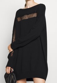 Pull noir surdimensionné avec des panneaux en dentelle sur le devant et les manches, doté d'une texture douce et de bords effilochés pour plus de détails.