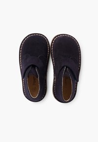 Chaussures en daim bleu marine avec un design à bout rond, des accents en cuir beige cousus, et une sangle en Velcro sur le dessus. Texture douce et style décontracté.