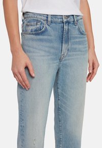Jeans in denim azzurro chiaro con una vestibilità rilassata, cinque tasche e lievi segni di usura all'orlo, con sfumature delicate e dettagli di cucitura.