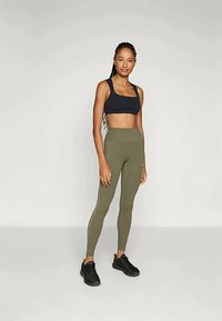 Sujetador deportivo negro y leggings de tiro alto en verde oliva con franjas laterales, combinados con zapatillas deportivas negras. Tejido suave y elástico.