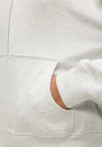 Ανοιχτό γκρι φούτερ με κουκούλα, κατασκευασμένο από απαλό ύφασμα, με τσέπη καγκουρό και ριμπ μανσέτες. Διαθέτει λεία υφή και διακριτική ραφή.