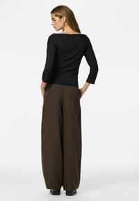 Top nero a maniche lunghe con scollo a barca abbinato a pantaloni marroni a vita alta e gamba larga. Tessuto liscio e vestibilità comoda.