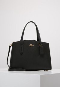Czarna skórzana torba na ramię o usztywnionej konstrukcji, z krótkimi uchwytami, odpinanym paskiem na ramię, złotymi akcentami oraz logo marki na przodzie.
