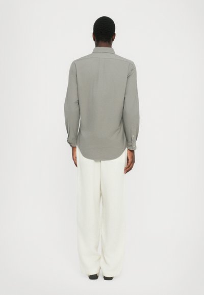 Siva dolgi rokav s sponko, zadaj s prelomom in zaobljenim robom, v kombinaciji z ohlapnimi belimi hlačami.