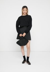 Maglione nero con "amore" in perline, gonna nera plissettata, borsa nera a forma di ventaglio, calzini neri e scarpe bicolore.