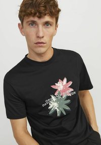 Camiseta de algodón negra con un diseño gráfico floral en rosa y verde, con texto blanco que dice "Originals ©1990 Design in Copenhagen".