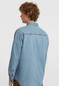 Light blue denim shirt with a classic collar, long sleeves, and buttoned cuffs; features a slightly textured fabric and back yoke detail.
