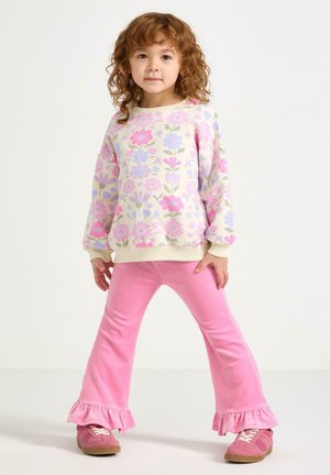 Sweatshirt med blomstret print i pastelfarver; cremefarvet bund med pink, blå og grønne blomster. Pink udflared bukser med flæsekant, båret med pink sko.