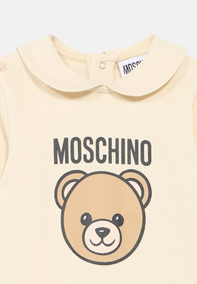Prenda para bebé de color crema con cuello redondeado, texto negro "MOSCHINO" y un gráfico de cara de oso de peluche en el frente.