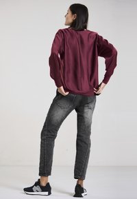 Burgundy satin top with long sleeves and fitted cuffs, paired with grey denim jeans and black sneakers with white accents.