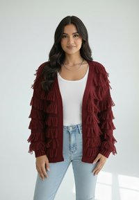 Bordowy sweter kardigan z dzianiny o fakturze z falbankami, z rozpiętym przodem, długimi rękawami i luźnym krojem, zestawiony z białym topem i jasnoniebieskimi dżinsami.