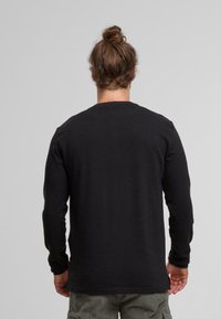 Langärmliges schwarzes Shirt, gerippte Textur, Rundhalsausschnitt, gerade geschnitten. Verfügt über verstärkte Nähte, lockere Passform und weichen Stoff.